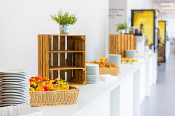 Buffet with fresh fruit in the foreground. Plates, some plants, and wooden boxes as decoration can be seen in the background in a bright and natural setting.