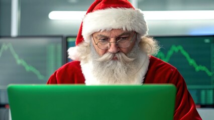 Santa in green business concept. Santa Claus working on a laptop in an office setting with stock market graphs in the background.
