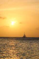 sunset off of Eagle Beach in Aruba with a sailboat on the horizon. landscape banner with copy space.