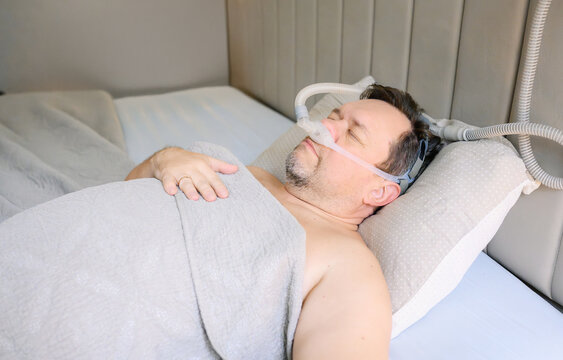 a middle-aged man relaxing in bed with cpap mask - Powered by Adobe