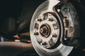 A close-up shot of a car's disc brake assembly, featuring a worn brake rotor, caliper, and lug studs on the wheel hub