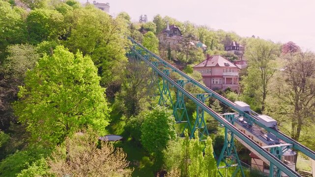 Drohnenflug &uuml;ber die Dresdner Bergbahn Schwebebahn  Bergbahn am Tag. Zwei Bahnen fahren aneinander vorbei, umgeben von viel Gr&uuml;n, B&auml;umen und einigen H&auml;usern am Hang.
