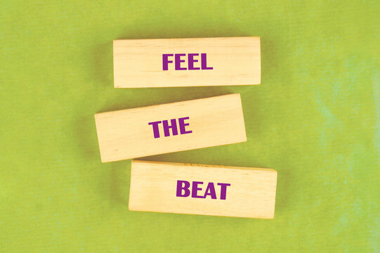 Three light wooden blocks with the words FEEL THE BEAT in purple font are staggered on a bright green background, urging viewers to connect with the rhythm and energy of sound