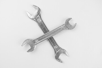 Close-up of two metallic wrenches crossed on a white background, highlighting their textured surface and industrial design, symbolizing tools, repair, and mechanical work.