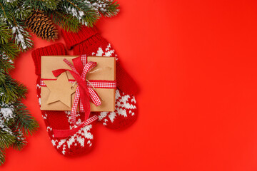 Gift box on winter mittens, snowy fir branches and red background