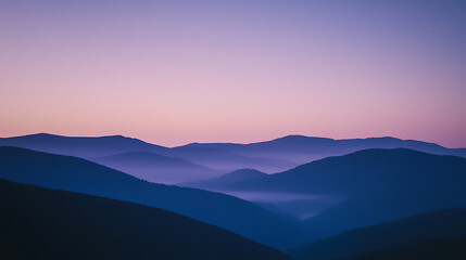Serene view of mountains at dusk with a soft lavender and pink sky. Layers of hills create depth, with a peaceful, misty valley between ridges, evoking tranquility.