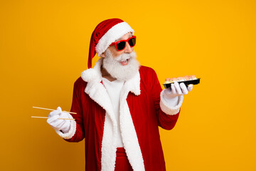 Santa Claus holding sushi while celebrating Christmas in a festive mood in front of a vibrant yellow background