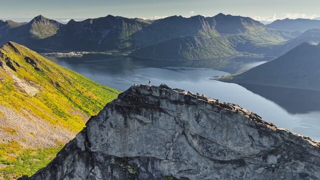 Hiker reach the summit and admire breathtaking views of mountains and water in Norway. Hiker on rocky peak overlooking calm waters and majestic landscapes Senja island, Norway