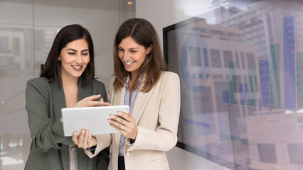 Obraz premium Two happy business women using tablet for sharing advice