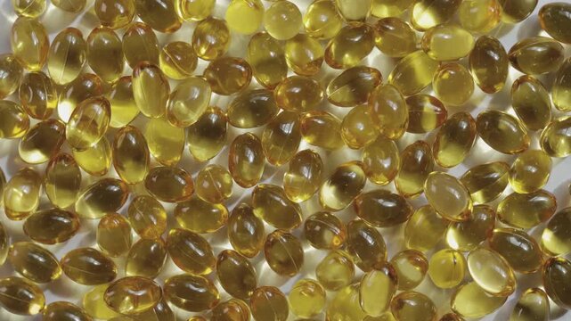 Top-down, close-up video of golden softgel capsules, like vitamin or fish oil supplements, slowly rotating on a turntable on white background showing concepts of healthcare, medicine, and nutrition.