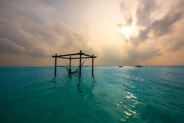 Tranquil closeup calm sea water waves with palm trees. Model sitting on hammock. Tropical island beach landscape exotic shore coast. Summer vacation, holiday amazing nature. Relax paradise, Maldives.