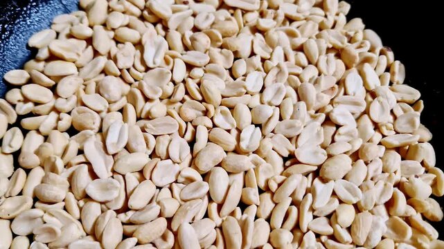 Macro top-down view of shelled and split peanuts filling a black textured pan. The static shot highlights the texture and detail of the legumes as a food ingredient for cooking or as a healthy snack.