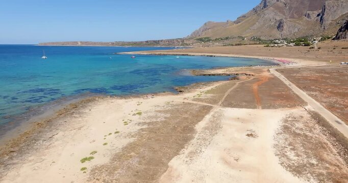 Aerial view of a stretch of rocky coastline in Sicily, Italy. A mountain in the background and the turquoise sea in the foreground.