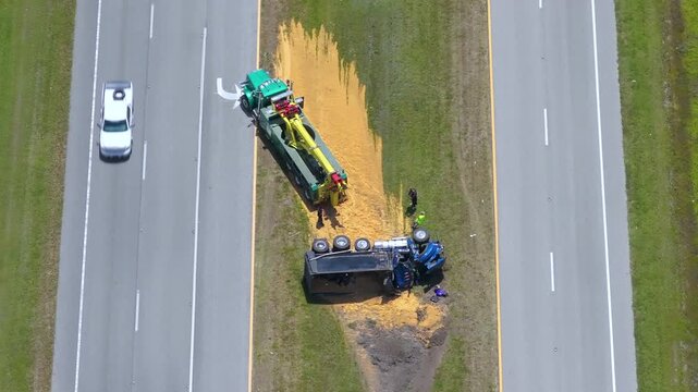 Rescue operation underway for tipped-over truck spilling dry goods on highway shoulder.