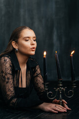 Mysterious young woman in black lace gazes intensely through candlelight, evoking elegance and gothic allure