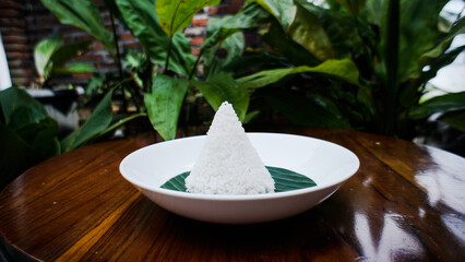 A close-up shot of a cone-shaped rice dish on a white plate with a green leaf.