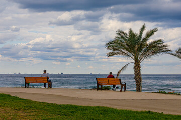 two people are sitting on benches on the seashore