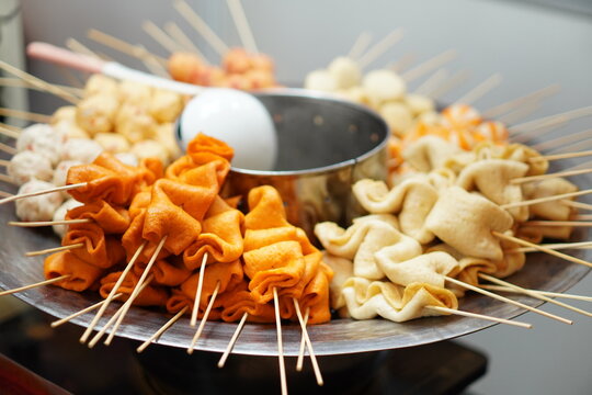 Close-up of assorted Korean odeng fishcakes on skewers at a street food stall. Various shapes and colors arranged around a steaming pot, ready to be cooked and served.