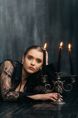 Mysterious young woman in black lace gazes intensely through candlelight, evoking elegance and gothic allure