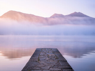 Stone jetty on misty lake with mountain backdrop mountains