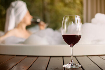 taça de vinho com mulher tomando banho de espuma ao fundo, momento de relaxamento e autocuidado íntimo