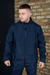 Fototapeta premium Stylish man in dark navy jacket poses confidently against a brick wall in an urban setting during daytime