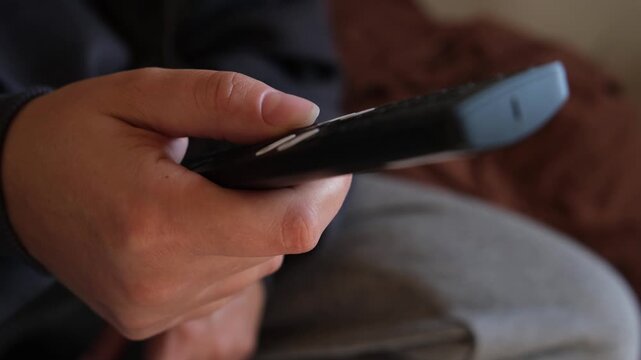 Clicking TV remote control with finger, close-up simple lifestyle scene