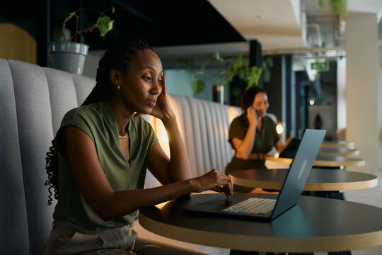 Stressed young black businesswoman in smart casual using laptop at desk in office lobby