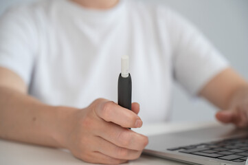 A woman smokes an electronic cigarette while working on a laptop. Tobacco heating system.