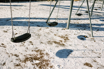 Empty swings sway in the winter snow at a local park during the afternoon