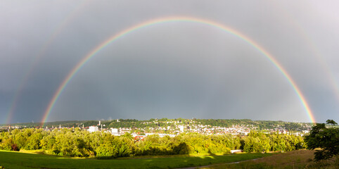 Stunning wide-angle shot of a double rainbow arching over the German city of Ravensburg under a dramatic grey sky
