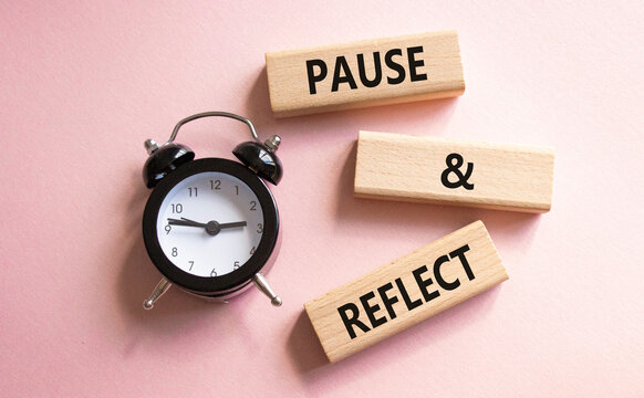 Pause and Reflect symbol. Concept words Pause and Reflect on wooden blocks. Beautiful pink background with alarm clock. Business and Pause and Reflect concept. Copy space.