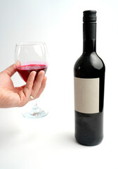 Hand holding glass of red wine beside bottle on clean white background, highlighting purity of composition, tasting moment, and minimalist elegance of refined presentation.