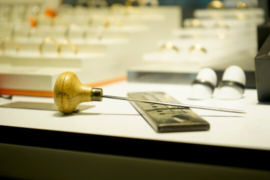Jeweler's awl with wooden handle on workbench beside metal ruler and rings, symbolizing craftsmanship, precision, and artisanal jewelry making in workshop light.