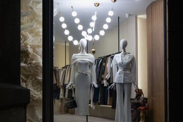 luxury fashion boutique window display at night with two mannequins dressed in elegant white and cream outfits, showcasing current winter collection and upscale style