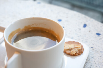 Cup of black coffee served with a small cookie.