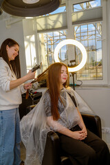 A hairdresser with an electric razor trims and conditions a female client's hair.