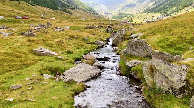 Flight over the narrow turbulent river flowing by the rocks. Some people take pictures on the boulders. The Carpathian Mountains, Romania.