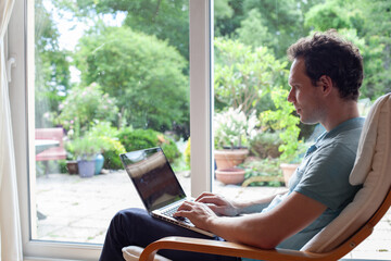 man working on laptop computer with empty screen at home, browsing internet website sitting in armchair indoors