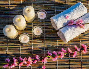 Spa arrangement with candles, towels, and pink flowers on a mat.