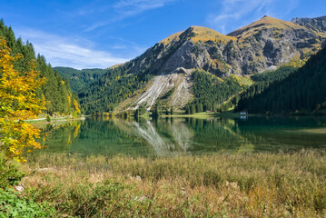 Vilsalpsee, Austria, showcasing clear mountain water, reeds, and a dramatic rocky slope.