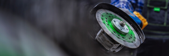 Construction worker with wearing protective gloves using an angle grinder with a spinning green disc for concrete. Concept industrial work, construction, renovation and engineering.