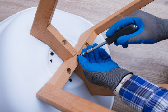 Close-up of a man assembling a wooden chair using a screwdriver. Concept of DIY home repair, furniture assembly, craftsmanship, and handyman work.
