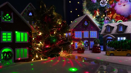 An evening Christmas village with a large Christmas tree and colorful houses with cars nearby