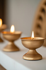 Illuminating golden bowls, each holding a soft flame that dances in the stillness. A line of light against soft background, symbolising warmth and peace. Reflecting glow on surface.