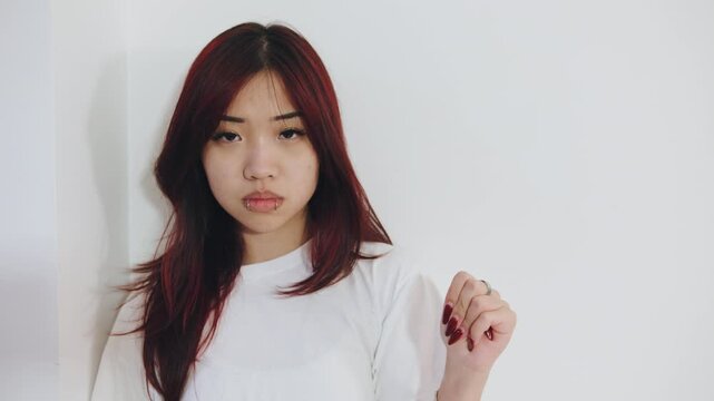 Young woman with long dark hair and red highlights showing four fingers folding over the thumb, the violence at home, signal for help, reflecting feelings of anxiety or tension
