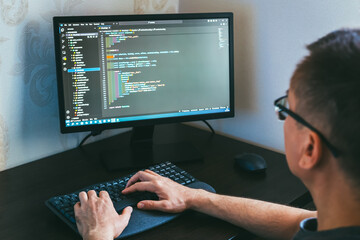 Remote work from home. Male programmer is engaged in coding on a computer, showcasing modern workspace with sleek monitor and keyboard, emphasizing concentration and digital environment