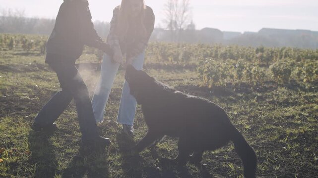 Dog trainer guides handler in working with a black shepherd in a field during a sunny day