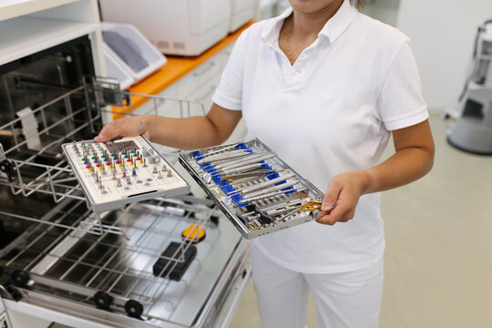 Hands of a dentist assistant carrying trays with cleaned drills and other tools.