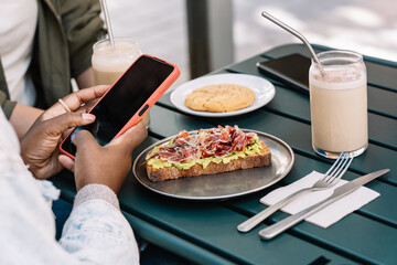 Multiethnic women enjoying brunch and using smartphone at cafe